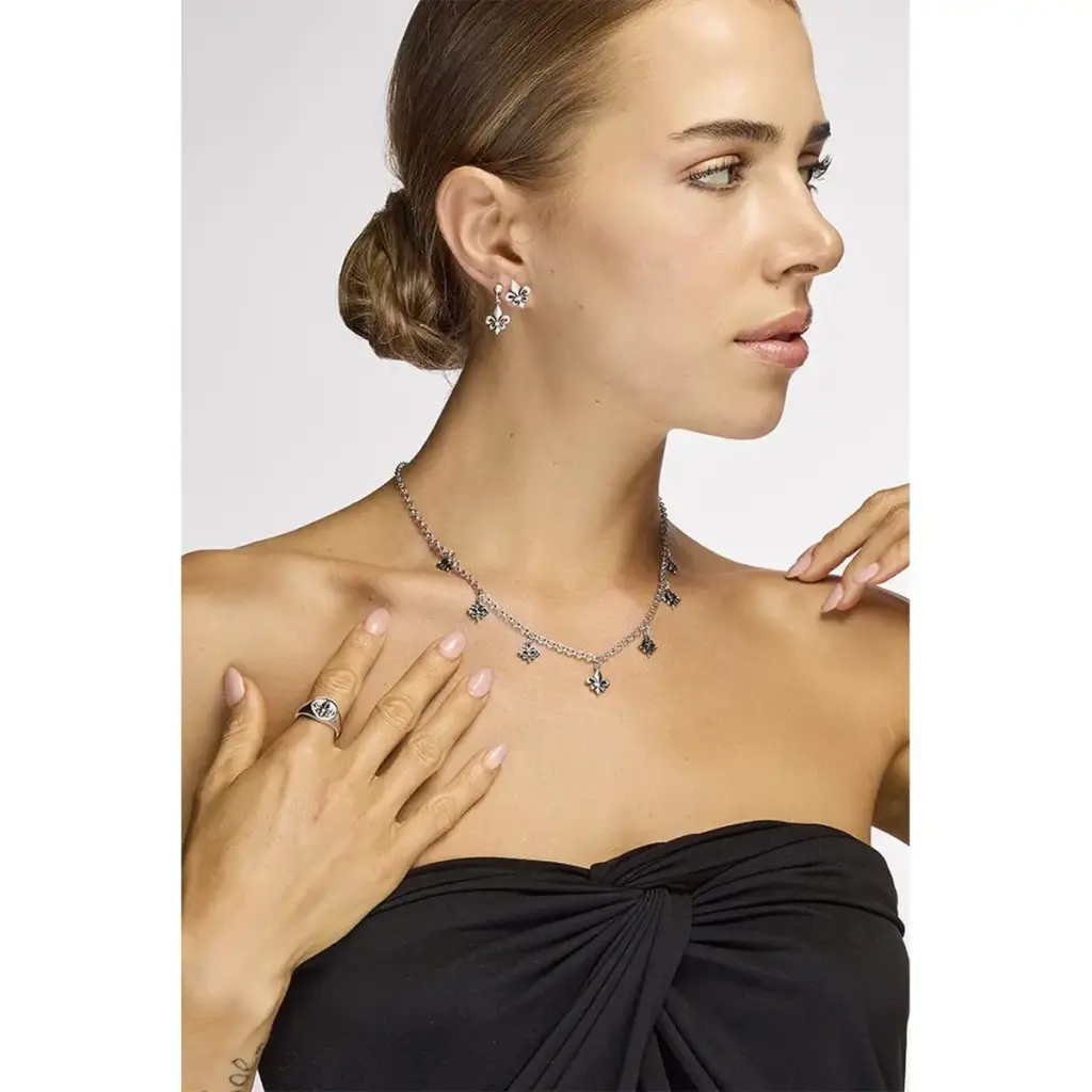 Ragazza con capelli raccolti in primo piano con top nero che indossa orecchini, collana e anello in argento con il simbolo del giglio
